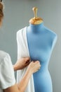 Seamstress measuring beautiful fabric on blue tailor dummy in her workshop. Royalty Free Stock Photo