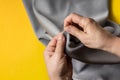 Seamstress`s hands on yellow tendy background. Female hands with a needle, thread and thimble. Woman sews grey clothes. Women`s