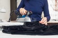 Seamstress steams a velvet jacket with an iron in her atelier. Authentic lifestyle