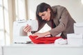 Seamstress works with red cloth. Young woman in formal clothes is indoors. Conception of style