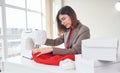 Seamstress works with red cloth. Young woman in formal clothes is indoors. Conception of style