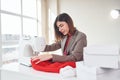 Seamstress works with red cloth. Young woman in formal clothes is indoors. Conception of style