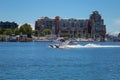 Seaplane landing on water with a port and buildings in the background under a blue sky in Canada