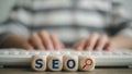 Search Engine Optimization (SEO) concept on wooden cubes with a woman using a computer keyboard Royalty Free Stock Photo