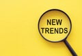 Searching new and popular trends. Magnifying glass over words on yellow background, top view Royalty Free Stock Photo