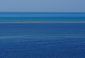 Seascape background with different shades of blue, a stripe of a small emerged sandy island in the middle and a distant ship