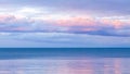 Seascape with blue ocean and pink hazy clouds floating above the horizon