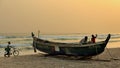 Sunset at a beach in ivory coast with a wooden boat on the sand and a boy walking with his cycle.