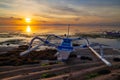 Seascape. Fisherman boat jukung on the sand during low tide. Rising sun at horizon. Traditional fishing boat at the beach during