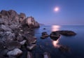 Seascape with moon and lunar path with rocks at night