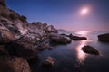Seascape with moon and lunar path with rocks at night