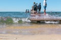 Seascape. Pier on coastline and waves on front focus, blurred people in the back. Beach vacation concept. Lifestyle