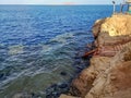 Seascape in Sharm El Sheikh Egypt and Tiran Island on the horizon. An old rusty metal staircase descends from a cliff to a coral Royalty Free Stock Photo