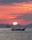 Tthai longtail boat in the sea at sunset with big red sun and mountains silhouettes and clouds Royalty Free Stock Photo