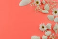 Seashells and flowers in shades of white forming a border on a coral colored background with copy space.