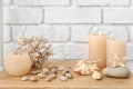 Seashells, pebbles and burning candles on table near white brick wall Royalty Free Stock Photo