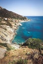 Seashore coastline with beach and rocks and rocky slope of the Island of Elba in Italy. Many people on the beach sunbathing. Blue Royalty Free Stock Photo