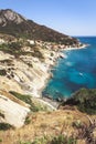 Seashore coastline with beach and rocks and rocky slope of the Island of Elba in Italy. Many people on the beach sunbathing. Blue