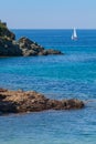 Seashore coastline with cliff and rocks on a mountain slope. Blue sea and a a sailboat in the background. Island of Elba in Italy