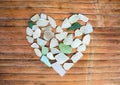 Seashore glass pebble heart on wooden background. Sugar glass mosaic for Valentine`s Day.