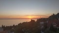 On the seashore there are pine trees and buildings. Fishing boats float on the water. In the autumn evening, the sun sets behind t