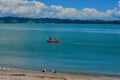 Seashores of New Zealand; beautiful seascape, bright blue ocean, and some people far away enjoying water activities.