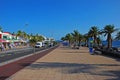 Seaside boulevard path quay of Puerto del Carmen town with rows of commercial shops, road and palm trees, Lanzarote island, Spain