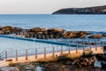 Seaside ocean swimming pool with metal hand rail fencing set against calm blue water and large exposed rocks