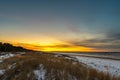 Seaside with sand dunes with snow and colorful sky with sun at sunset, sunrise Royalty Free Stock Photo