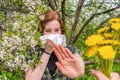 Season allergy to flowering plants pollen. Young woman with paper handkerchief covering her nose in garden and doing stop sign to Royalty Free Stock Photo