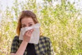 Season allergy to flowering plants pollen. Young woman with paper handkerchief in hand covering her nose in garden. Teen girl Royalty Free Stock Photo