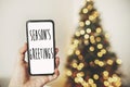 Season`s greetings text on phone screen on background of golden Royalty Free Stock Photo