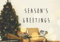 Season`s greetings text sign on christmas tree in golden lights bokeh with festive stylish gifts in white room. Seasons greeting