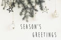Season`s greetings text sign on stylish christmas branches with glass modern ornaments hanging on white wall. Creative christmas