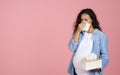 Pregnant woman suffering from snotty nose, pink background