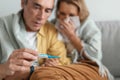 Seasonal flu. Worried senior man taking care of his ill wife at home, looking at thermometer with shock, selective focus Royalty Free Stock Photo