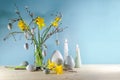 Seasonal holiday decoration with candles, a bouquet of daffodils and spring branches in a glass vase and artificial gray Easter