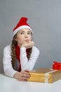 Seasonal Holidays and Christmas Ideas. POrtrait of Thoughtful Thinking Caucasian Female Girl in Santa Hat and White Shirt Holding Royalty Free Stock Photo