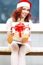 Seasonal Holidays Concepts. Portrait Lovely  Cute Caucasian Santa Helper Girl Posing in Santa Hat Offering Christmas Gift Box. Royalty Free Stock Photo