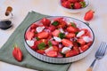 Seasonal salad with strawberries, tomatoes, soft cheese and chives flowers in a white plate on a light concrete background. Royalty Free Stock Photo