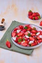 Seasonal salad with strawberries, tomatoes, soft cheese and chives flowers in a white plate on a light concrete background. Royalty Free Stock Photo