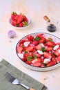 Seasonal salad with strawberries, tomatoes, soft cheese and chives flowers in a white plate on a light concrete background. Royalty Free Stock Photo