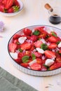 Seasonal salad with strawberries, tomatoes, soft cheese and chives flowers in a white plate on a light concrete background. Royalty Free Stock Photo