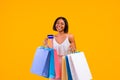 Seasonal shopping. Smiling black woman holding gift bags and credit card, smiling at camera on orange studio background Royalty Free Stock Photo