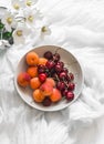 Seasonal summer dessert - apricots and cherries in a bowl and garden flowers in a jug on a white background, top view