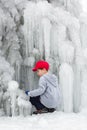 Seasonal winter mood, attractive frozen waterfall, iciles, young boy in red cap plays. Royalty Free Stock Photo