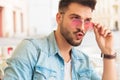 Seated astound man fixing sunglasses and looking to side Royalty Free Stock Photo