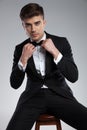 Seated handsome man in black tuxedo fixing his bowtie