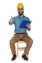 Seated happy engineer showing ok gesture while holding a clipboard