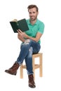 Seated happy man holding book in hand with legs crossed